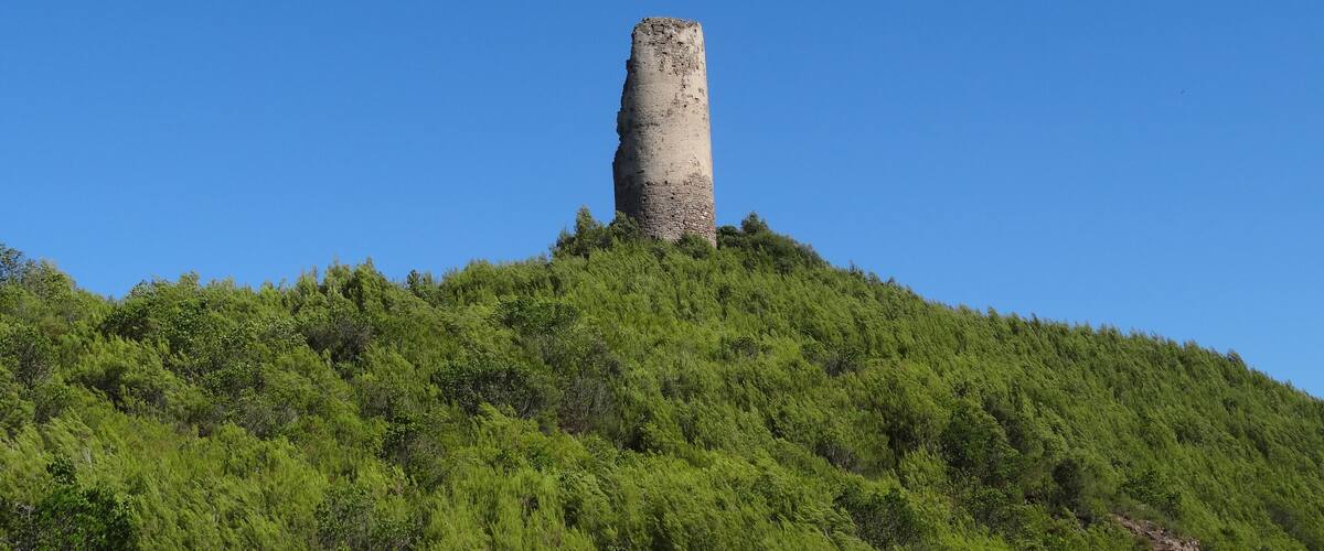 A tall, ancient stone tower on a green hill under a clear blue sky.