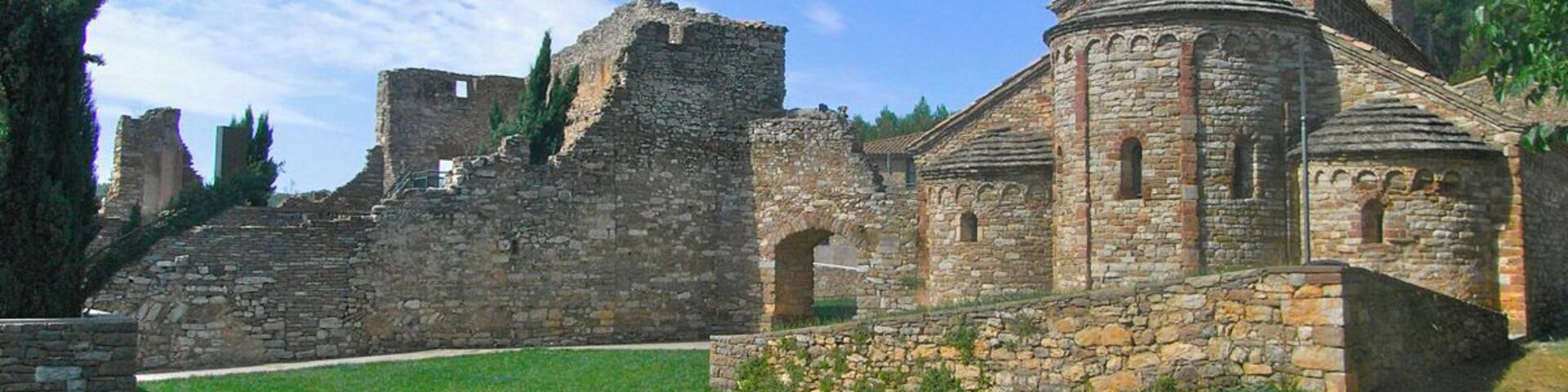 An ancient stone church with a bell tower and ruins in the background.