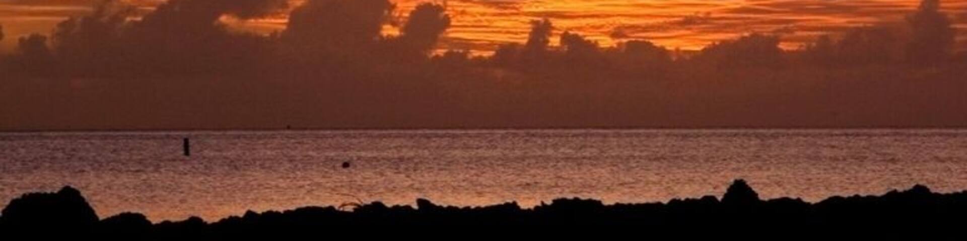 A sunset over a body of water with a rocky shoreline.