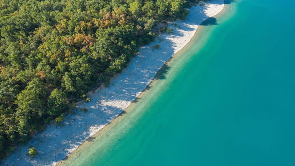 An aerial view of a beach with clear turquoise waters and a dense forest on one side.