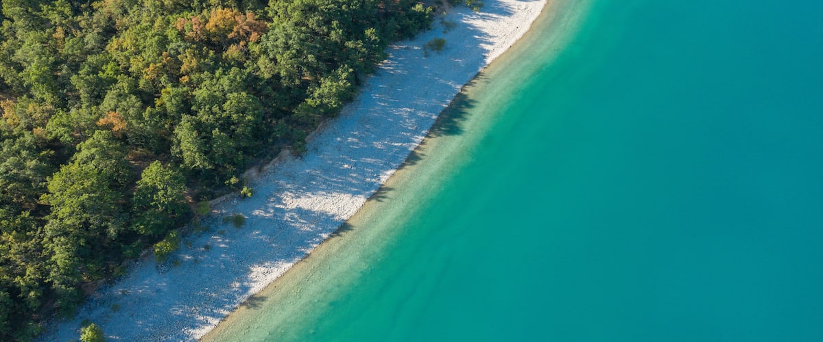 An aerial view of a beach with clear turquoise waters and a dense forest on one side.