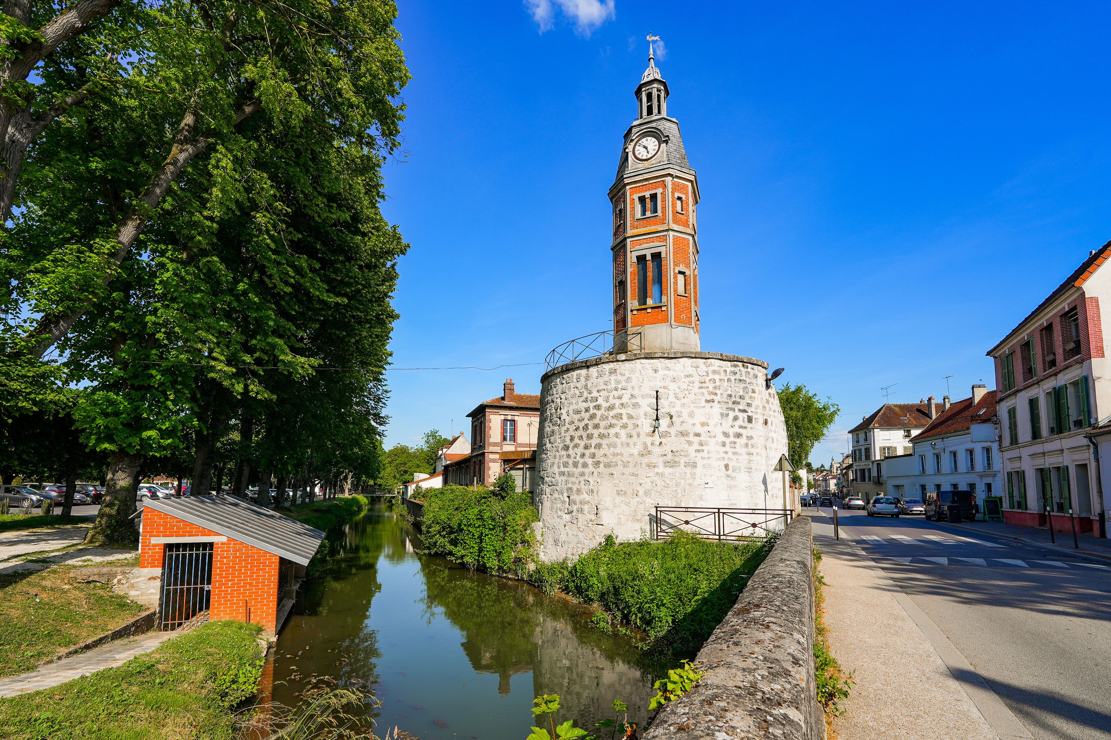 A historic tower with a clock, surrounded by a canal and lush greenery.