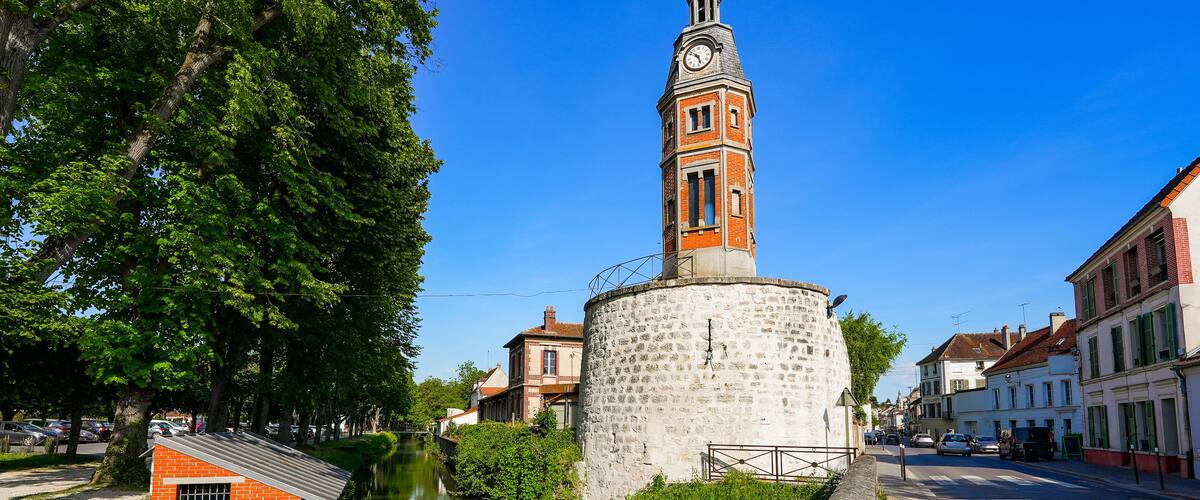A historic tower with a clock, surrounded by a canal and lush greenery.