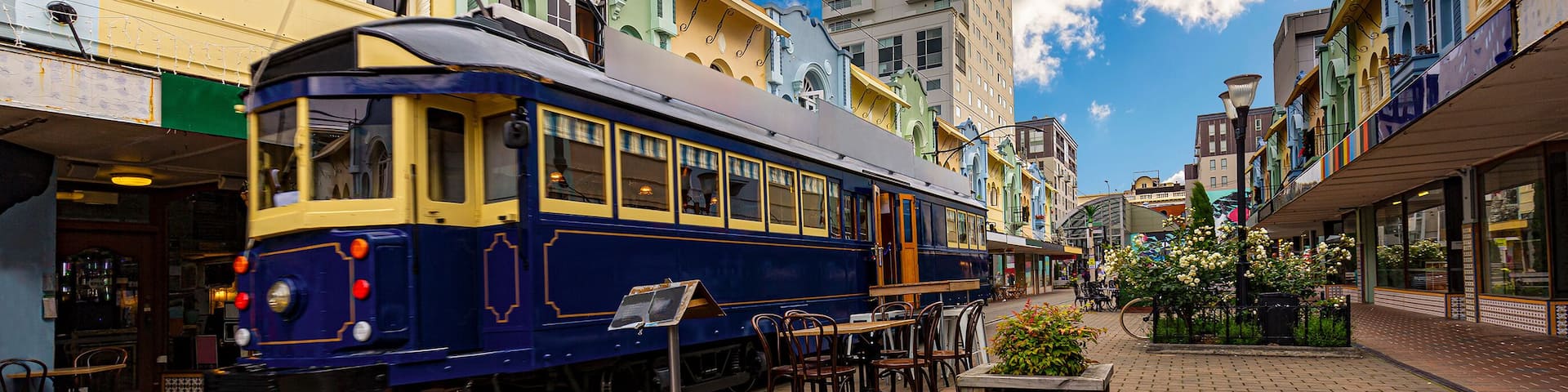 A tram on a brick-paved street with colorful buildings and a clear sky.