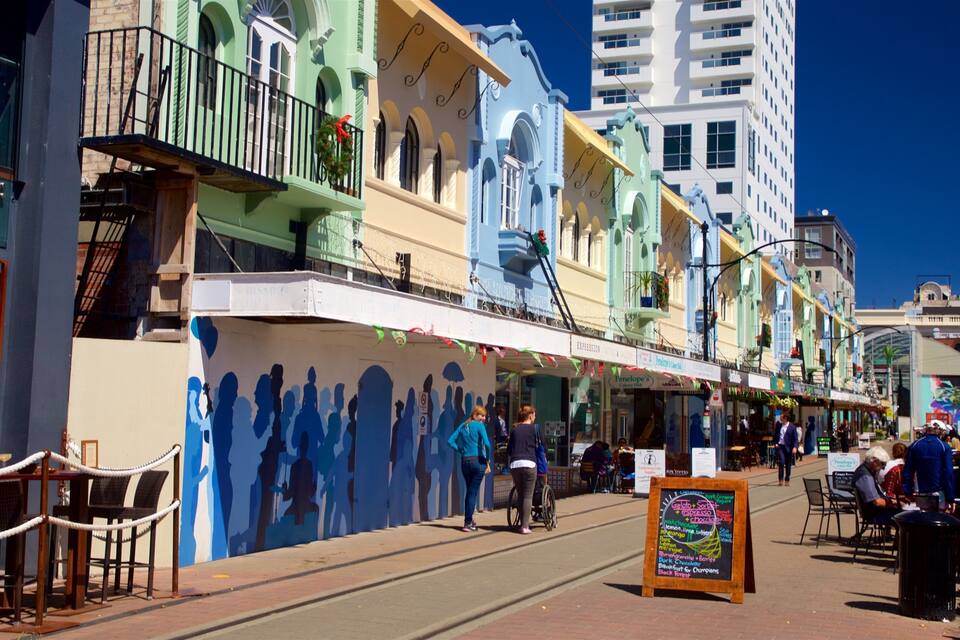 A vibrant street with colorful buildings, a mural, and outdoor seating areas.