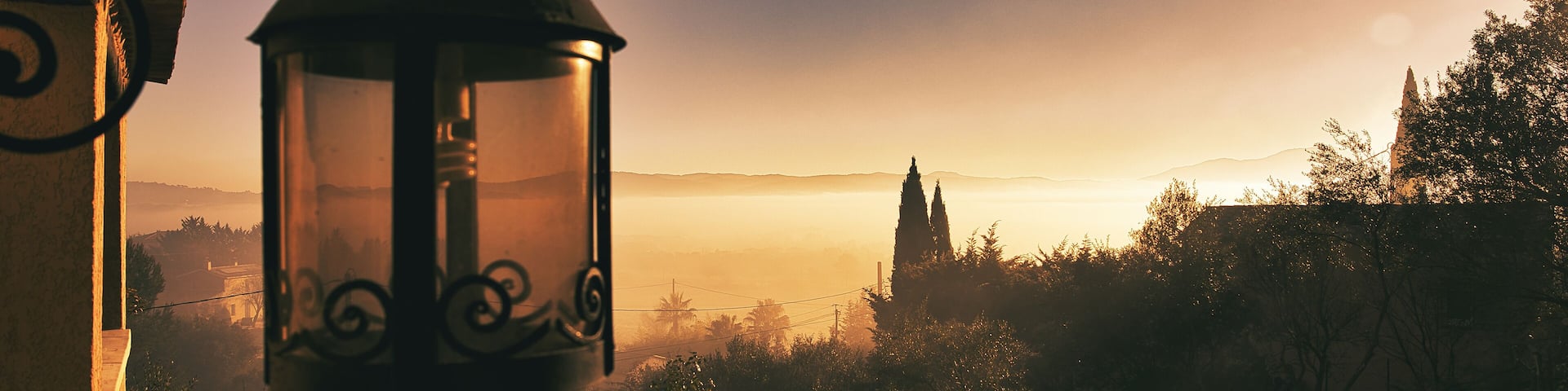 A lantern hanging indoors with a view of a distant landscape during sunrise or sunset.