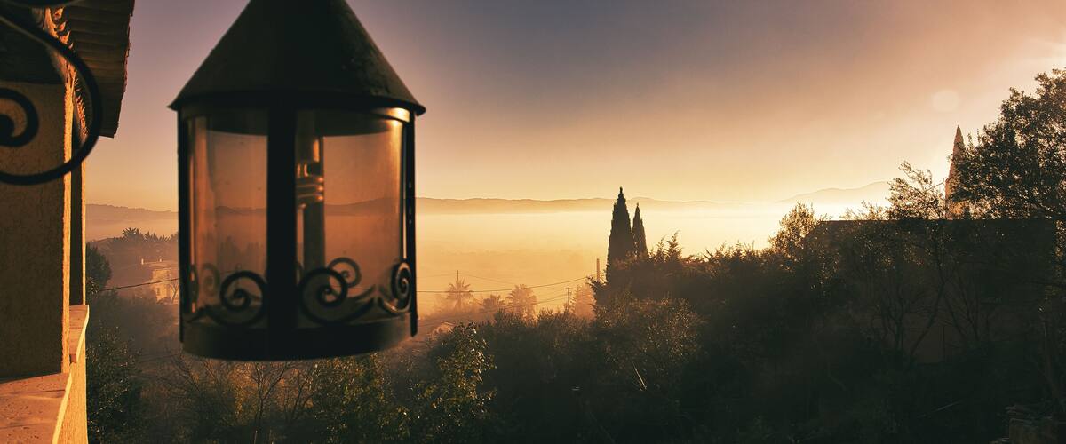 A lantern hanging indoors with a view of a distant landscape during sunrise or sunset.
