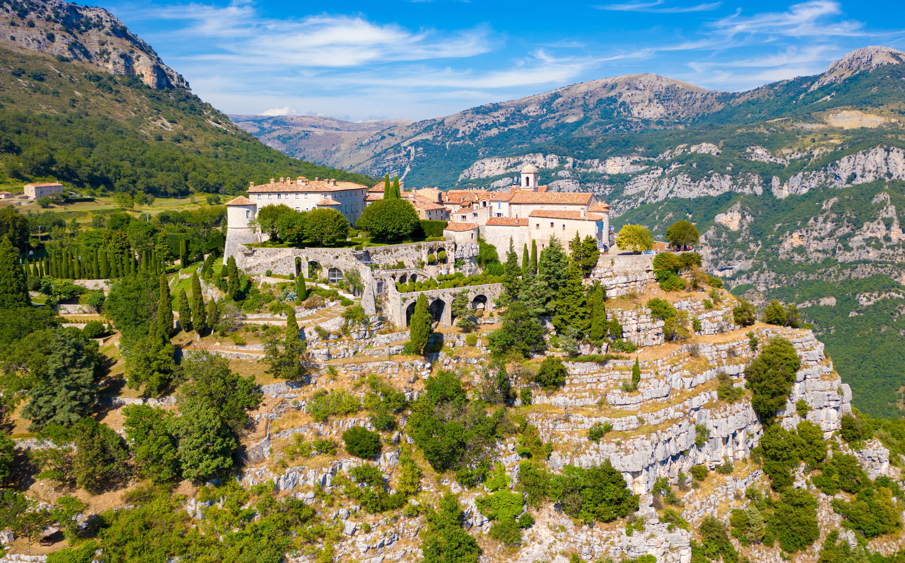 A historic building complex on a hillside with surrounding mountains and trees.