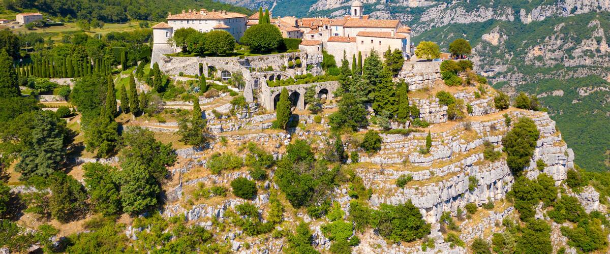 A historic building complex on a hillside with surrounding mountains and trees.