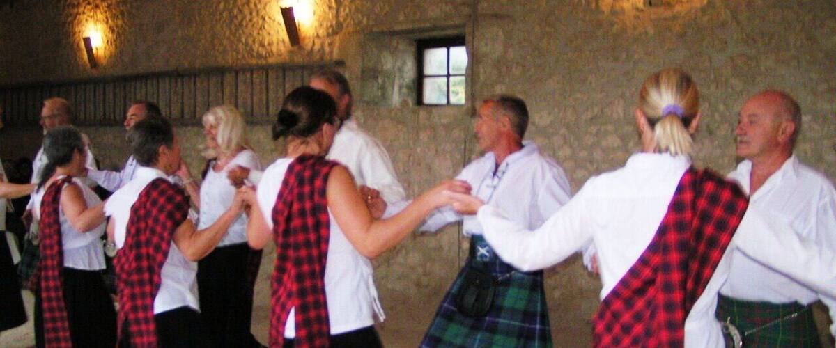 A group of people in traditional Scottish attire dancing in a stone-walled room.