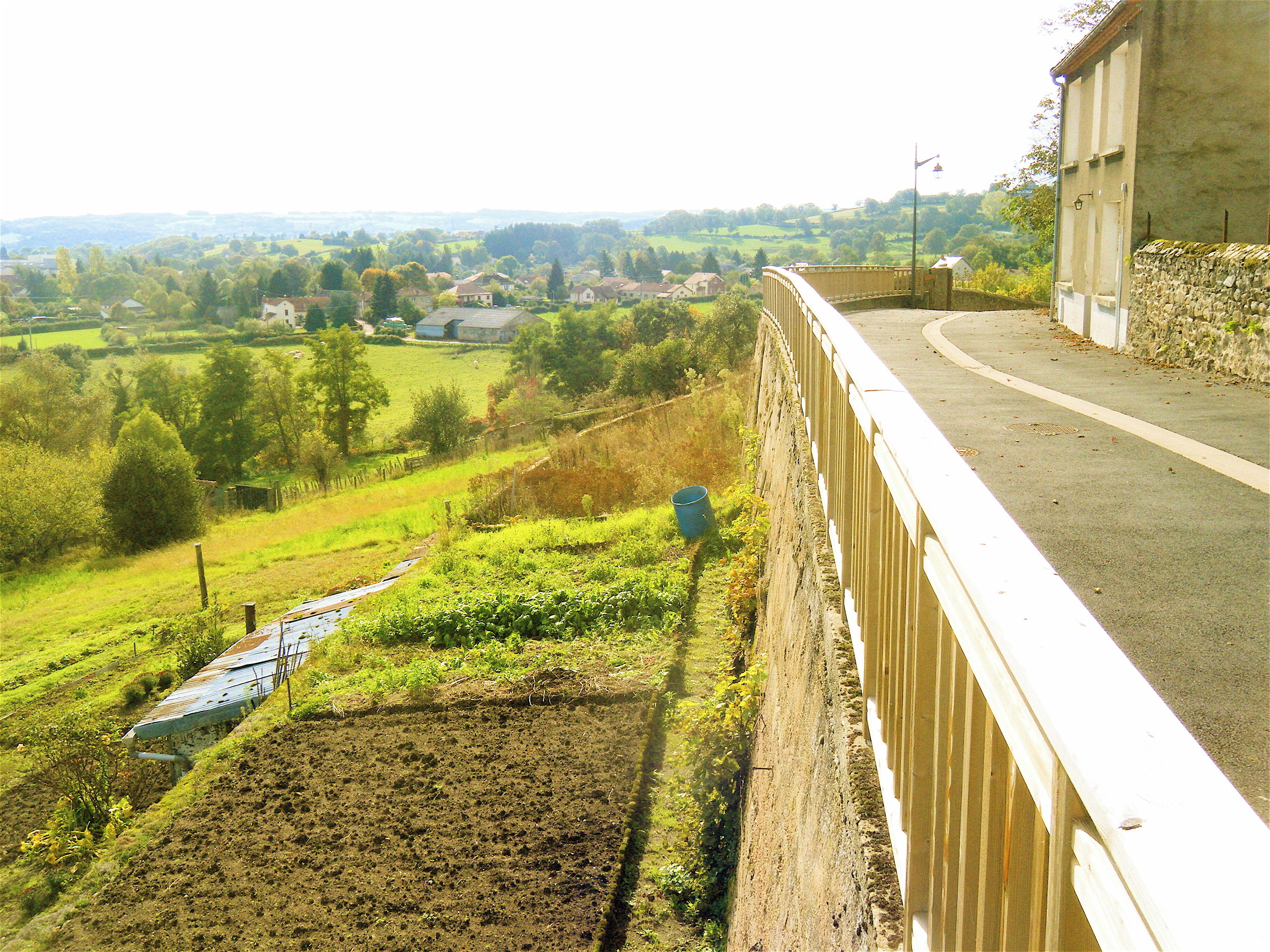 A rural landscape with a road alongside a stone wall, fields, and scattered houses.