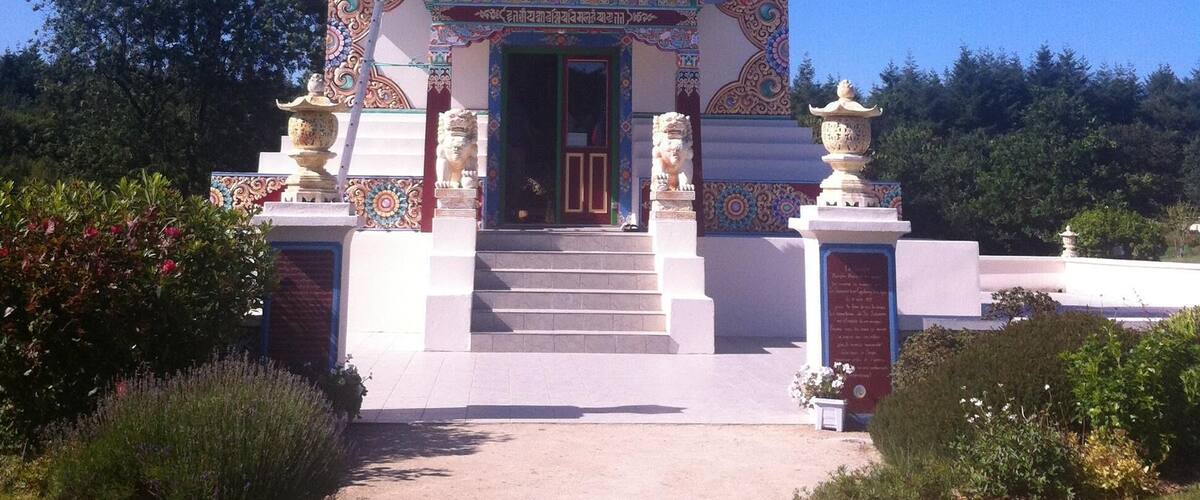 A colorful stupa with intricate designs and a statue on top, surrounded by a pathway and greenery.