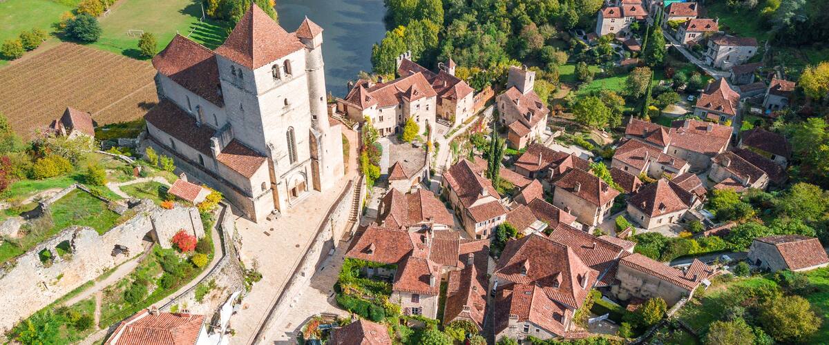An aerial view of a historic town with a prominent church tower, surrounded by traditional buildings and a river.