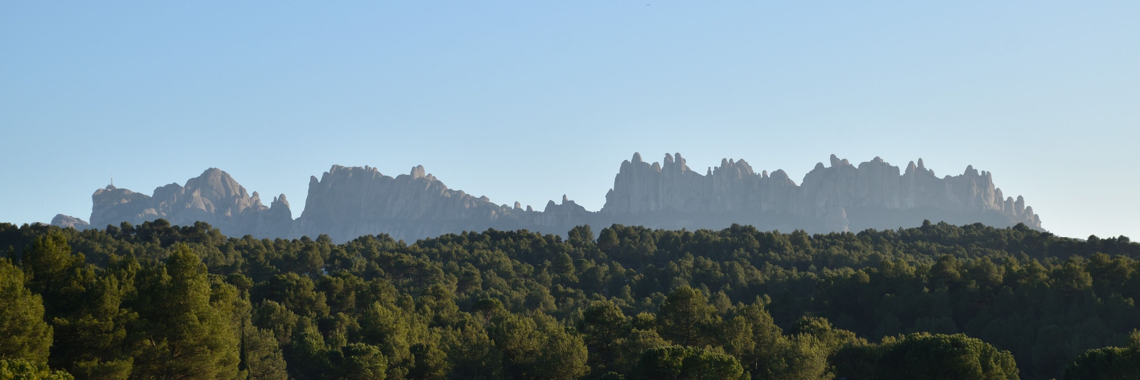 A forested hill with a range of rocky peaks in the background.