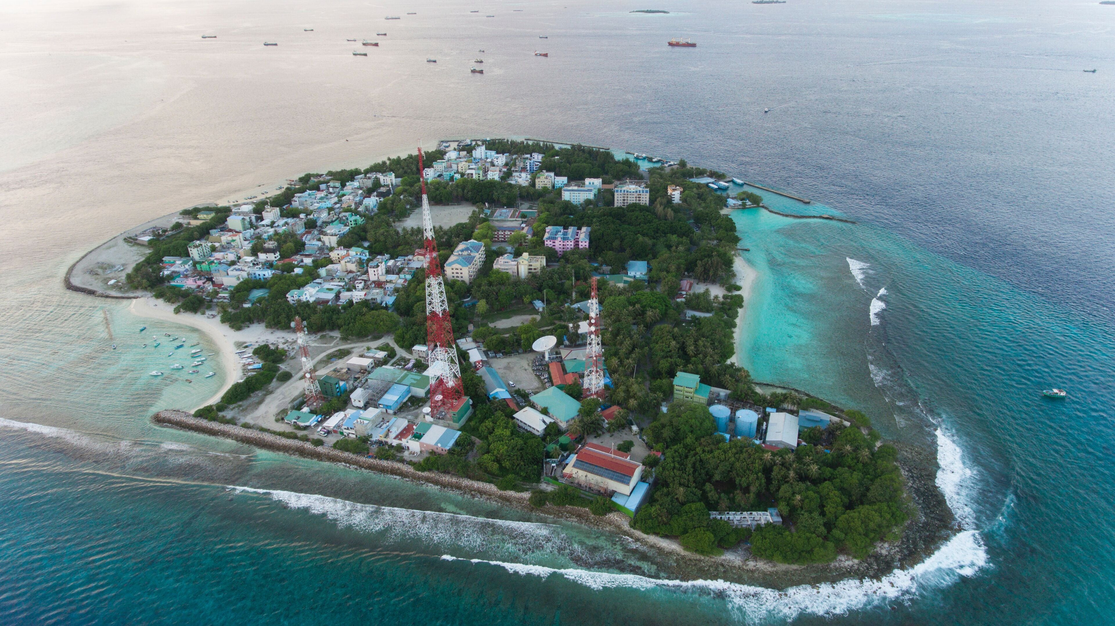 An aerial view of a coastal island with buildings, a lighthouse, and a clear blue sea.