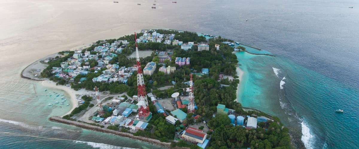 An aerial view of a coastal island with buildings, a lighthouse, and a clear blue sea.