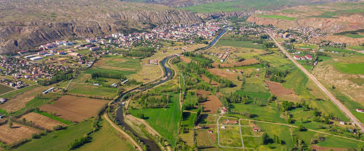 An aerial view of a town nestled in a valley with a river running through it, surrounded by green fields and mountains in the background.