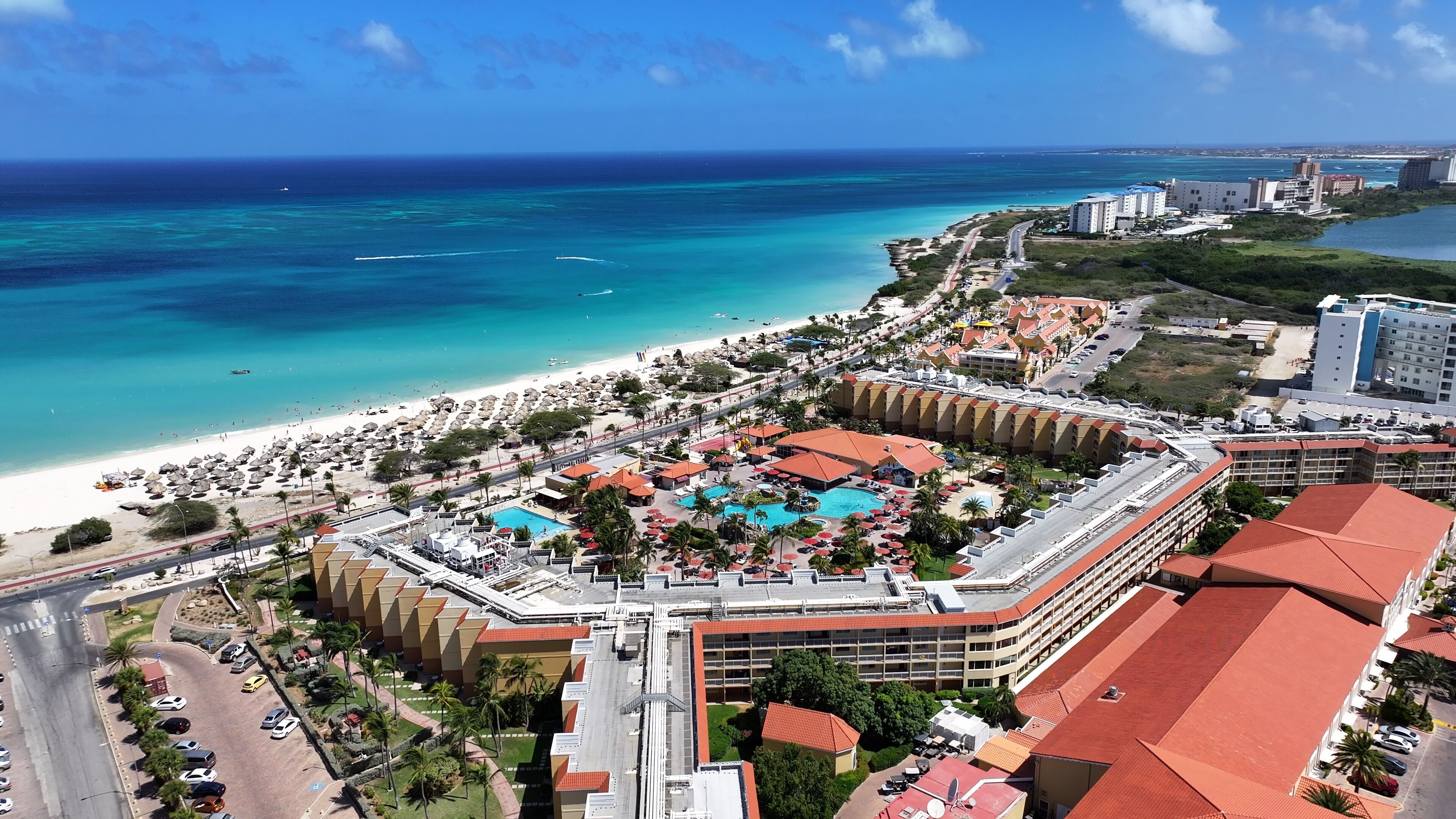 A coastal resort with a beach, swimming pool, and hotel buildings.