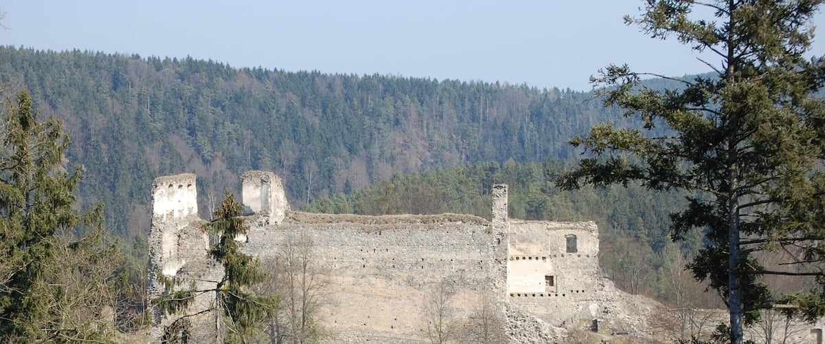 A historical stone castle ruins surrounded by dense forest and hills.