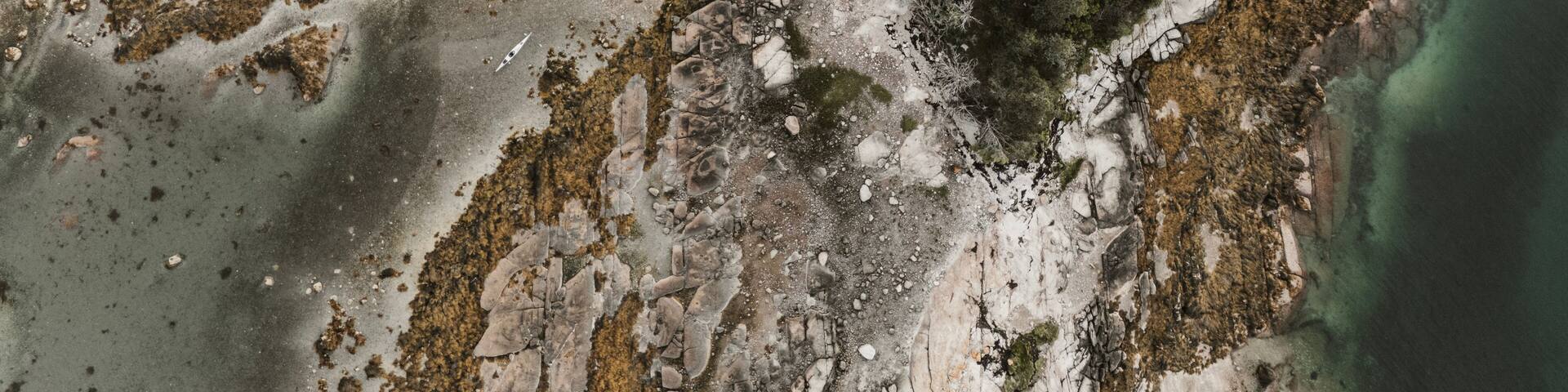 A coastal landscape with rocky terrain, sparse vegetation, and clear water.