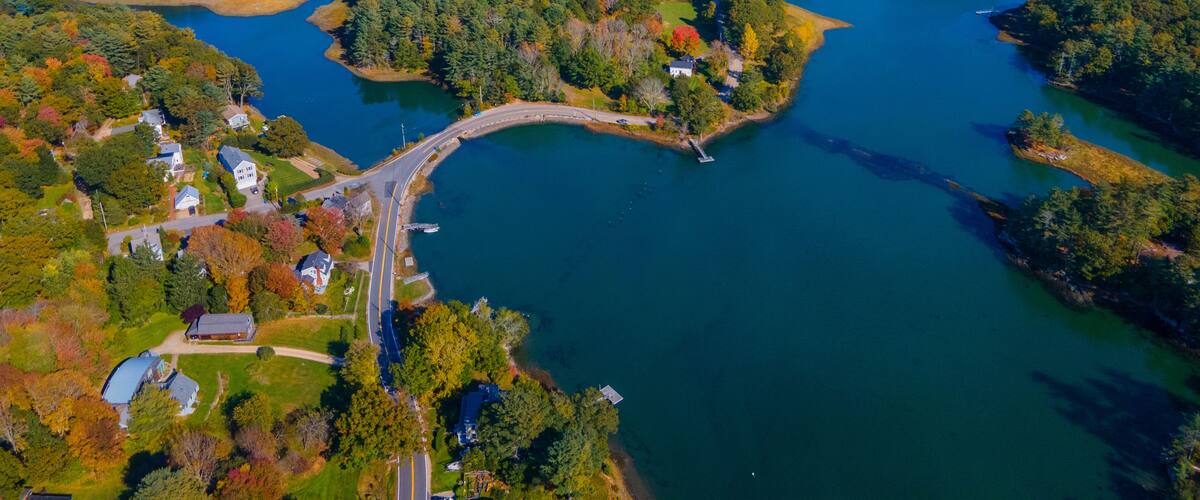 An aerial view of a coastal area with a bridge connecting two landmasses, surrounded by dense forests and a large body of water.