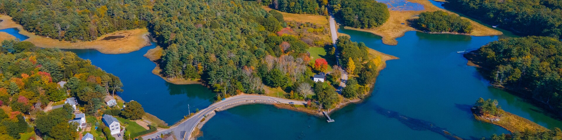 An aerial view of a coastal area with a bridge connecting two landmasses, surrounded by dense forests and a large body of water.