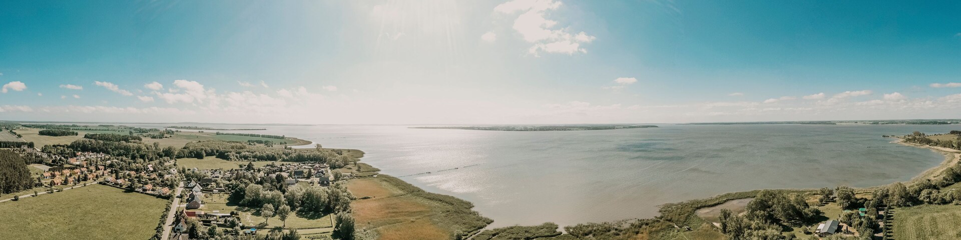 Vista panorámica de un pueblo costero con un río, campos verdes y casas dispersas.