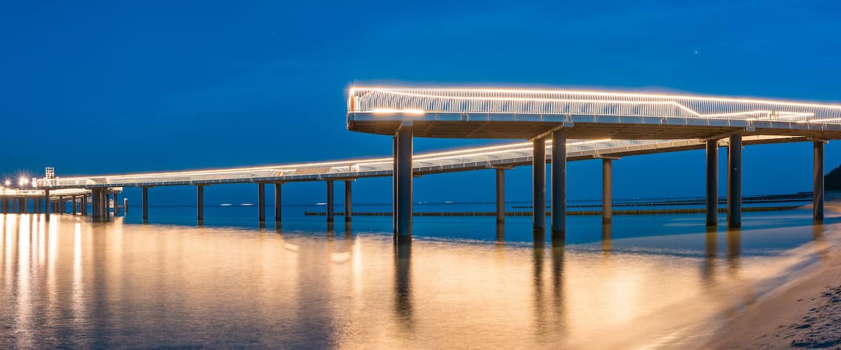 A long, illuminated bridge extending over calm water at night.