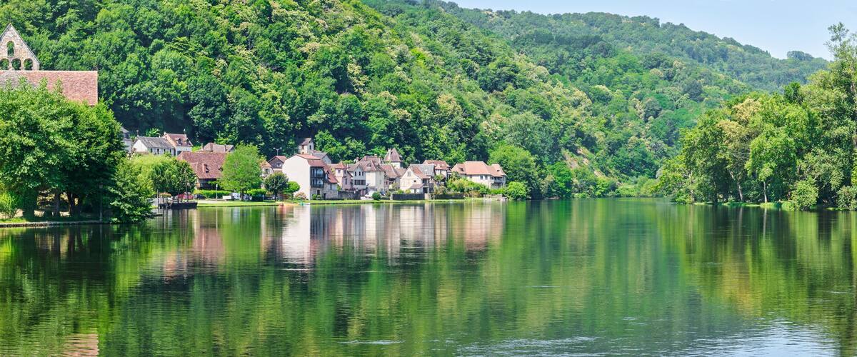 A calm lake with a village on the left, surrounded by lush green hills.