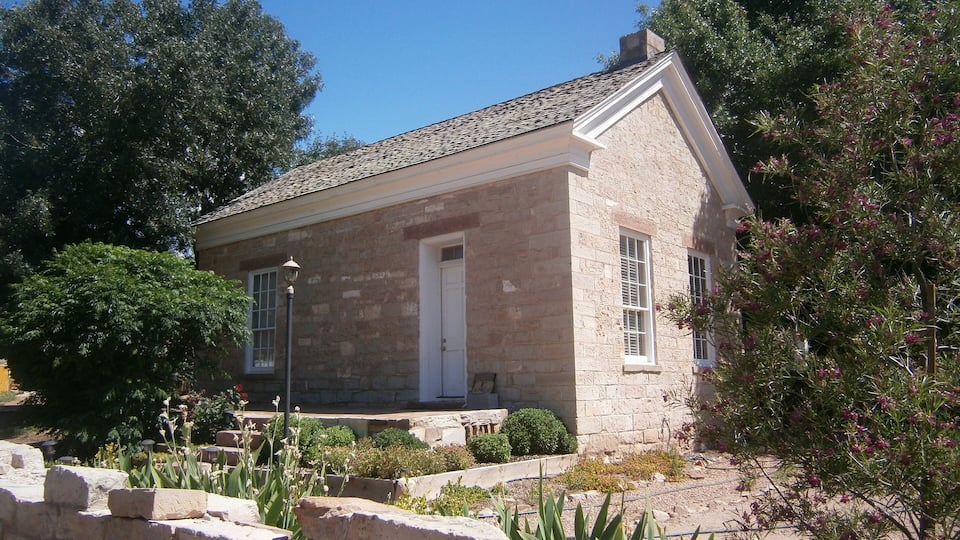A stone building with a tiled roof, surrounded by greenery and a stone wall.