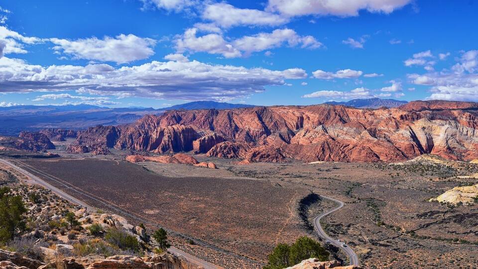 A canyon landscape with a winding road, red rock formations, and a clear blue sky.