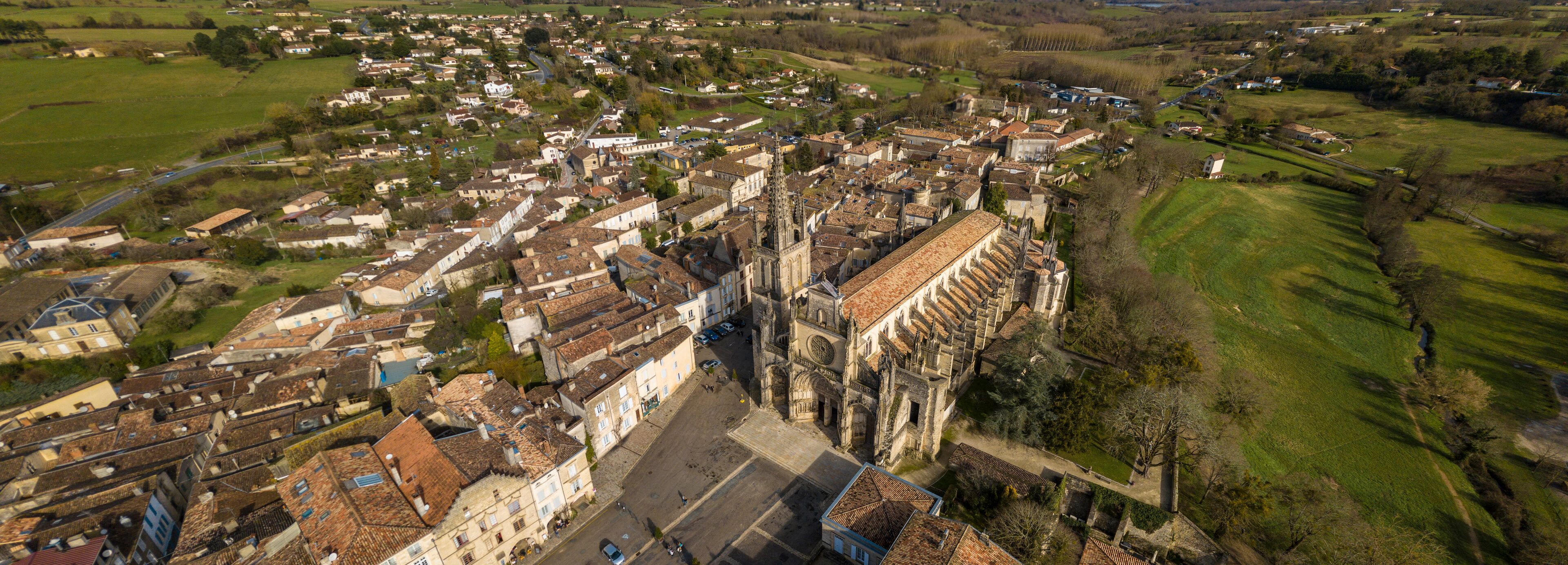 An aerial view of a historic town with a prominent cathedral, surrounded by residential areas and green fields.