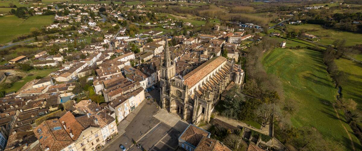 An aerial view of a historic town with a prominent cathedral, surrounded by residential areas and green fields.