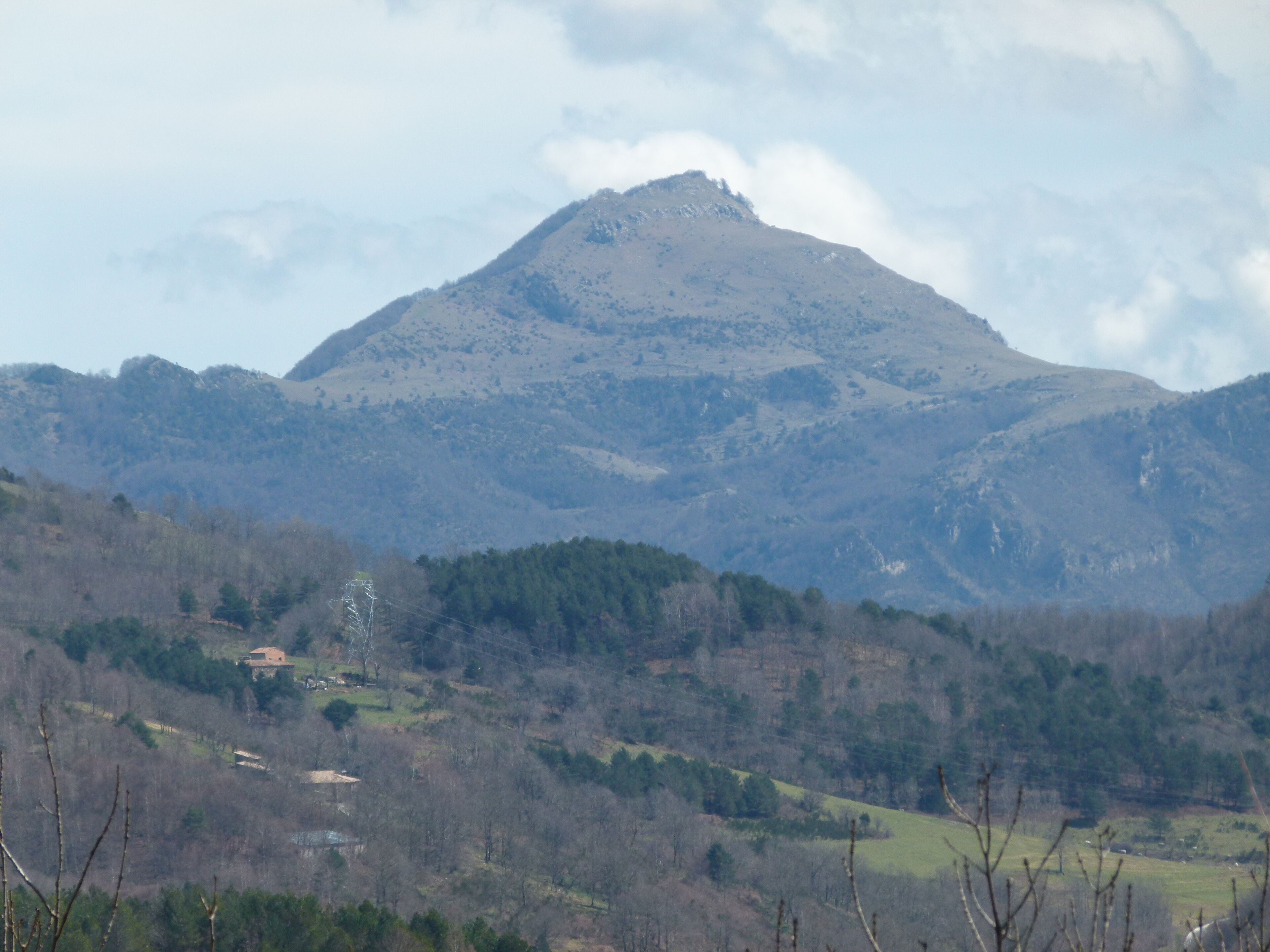 A mountain range with a prominent peak, surrounded by forested hills and a small building in the valley.