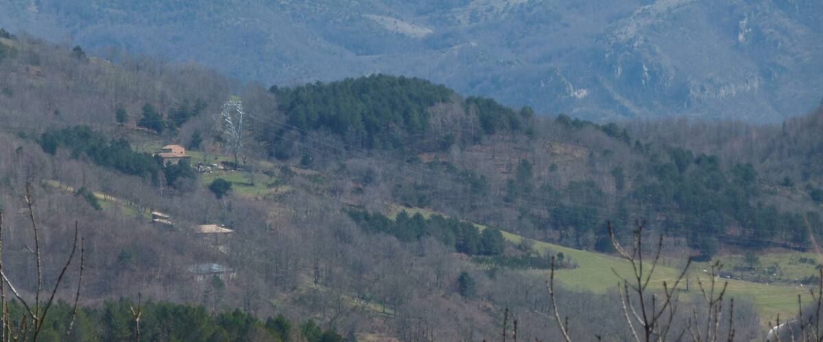 A mountain range with a prominent peak, surrounded by forested hills and a small building in the valley.