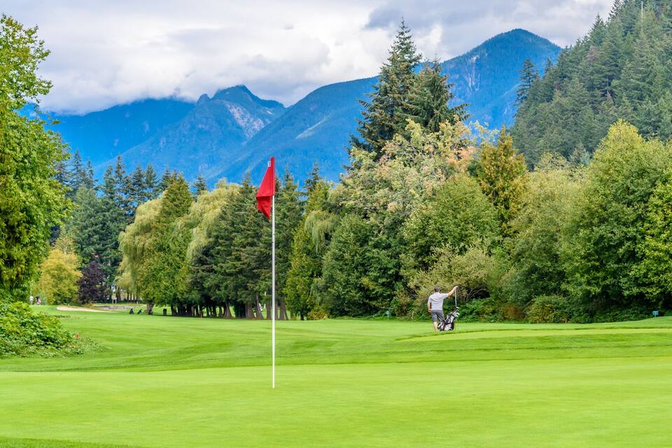 Un terrain de golf avec un drapeau rouge, un golfeur au loin et une chaîne de montagnes en arrière-plan.