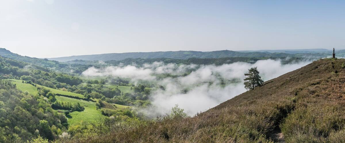 A mountain peak with a monument, surrounded by lush greenery and a valley shrouded in mist.
