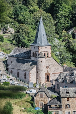 Una iglesia histórica con una torre destacada, rodeada de exuberante vegetación y edificios de piedra tradicionales.