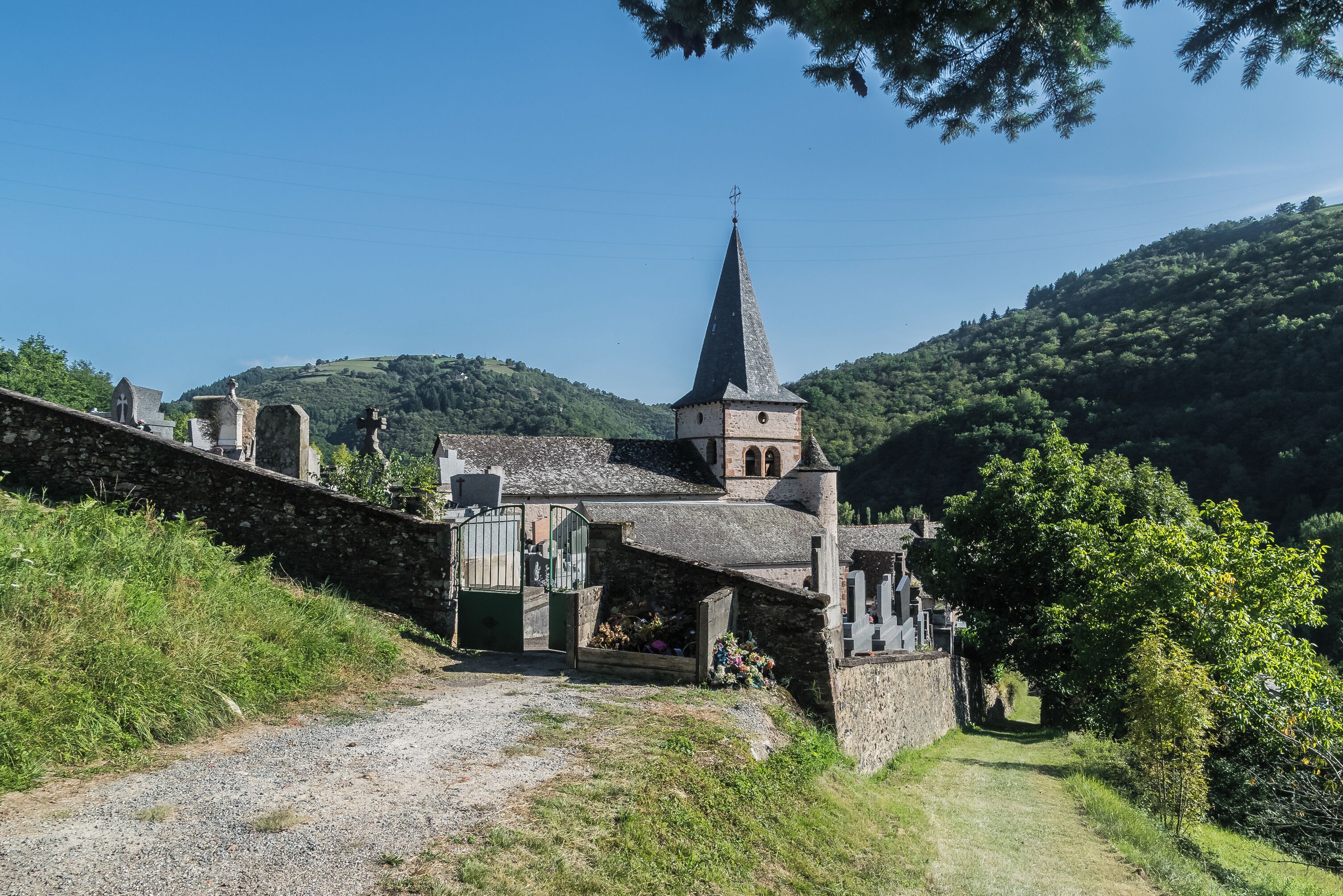 A church with a tall spire, surrounded by greenery and hills.