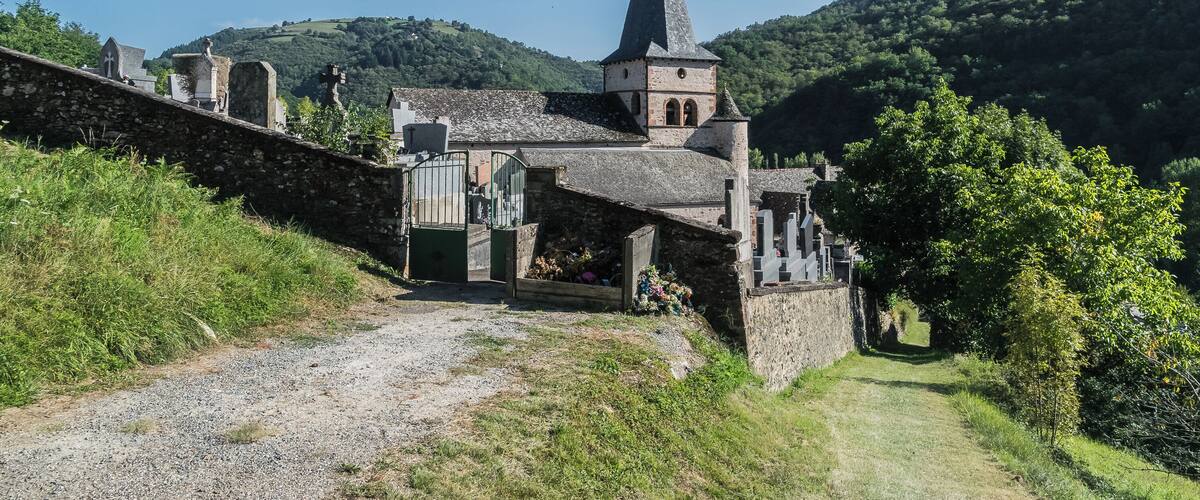 A church with a tall spire, surrounded by greenery and hills.