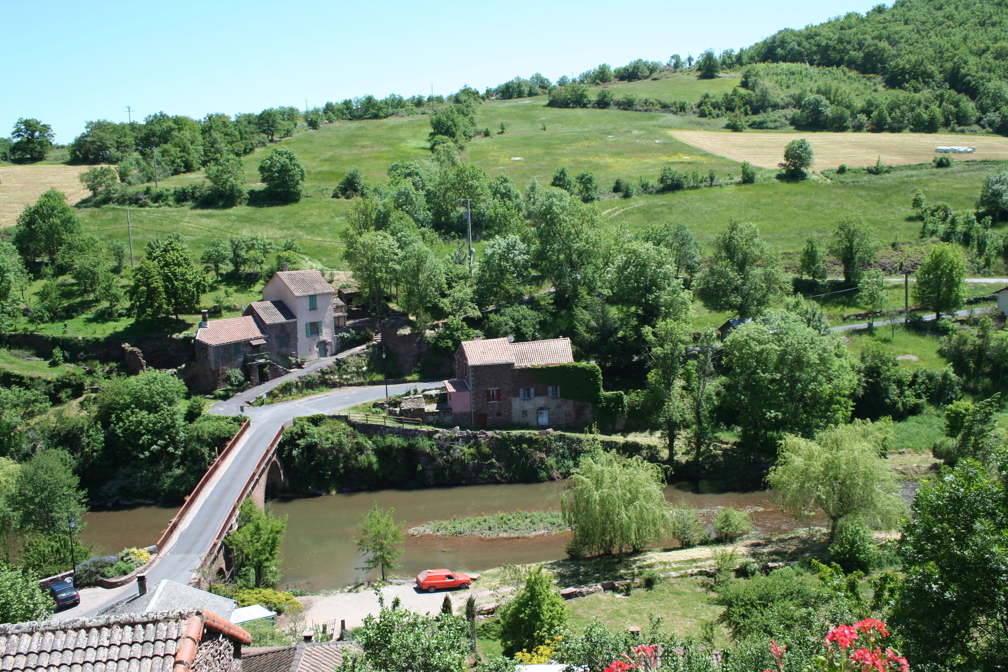 A rural landscape with a river, a bridge, and houses surrounded by greenery.