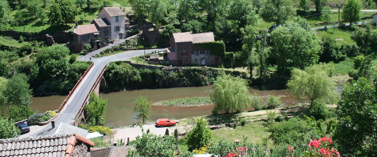 A rural landscape with a river, a bridge, and houses surrounded by greenery.