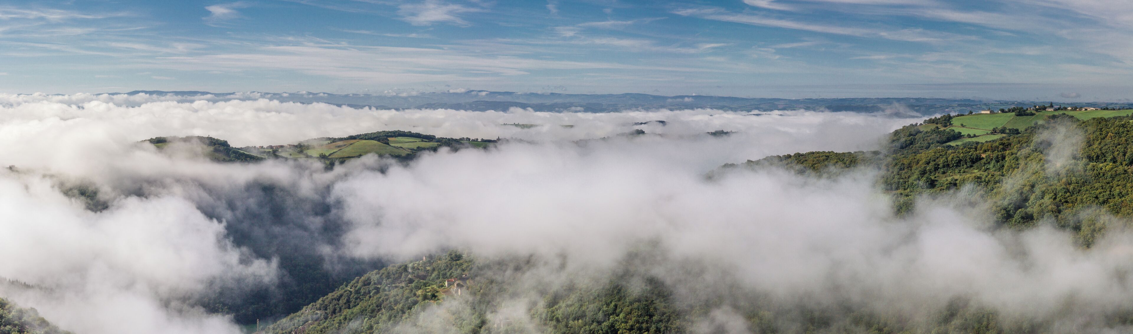 A valley with lush green hills and a blanket of clouds above.