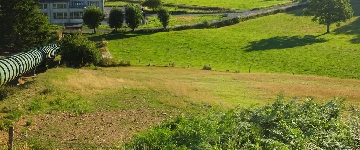 A rural landscape with rolling hills, a large white building, and a green field.