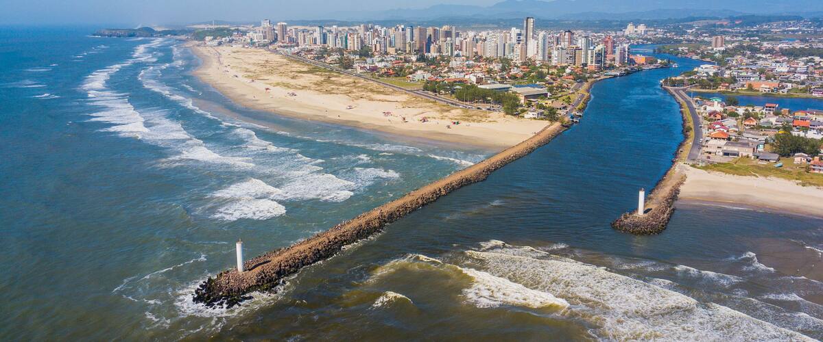 A coastal city with a beach, a long pier, and high-rise buildings.