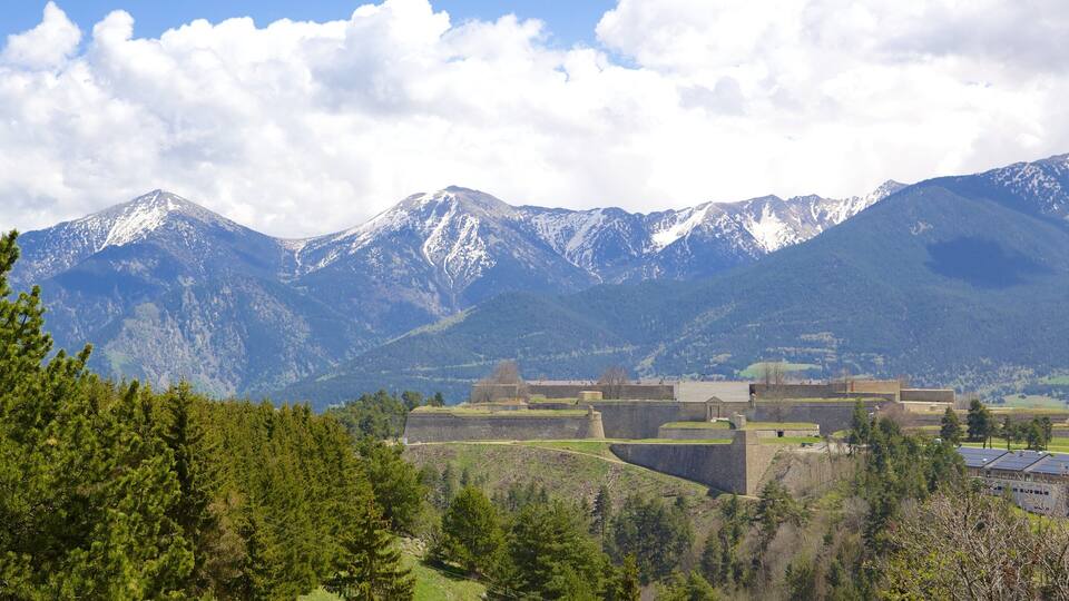A mountainous landscape with snow-capped peaks, a historic fort, and dense forests.