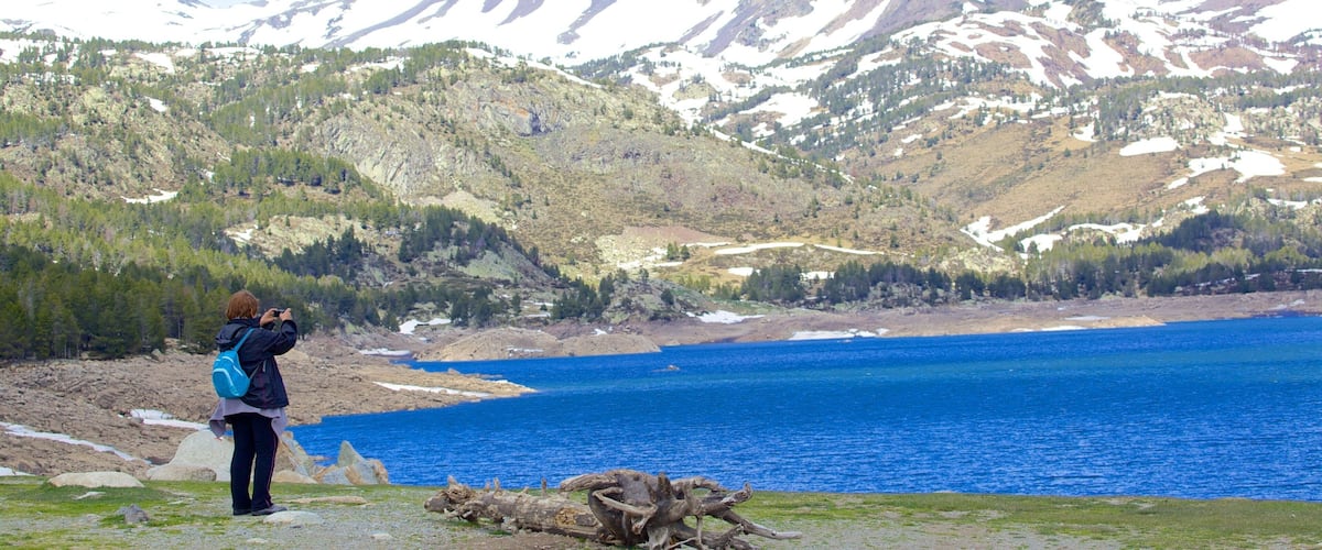 A person taking a photo of a mountain range and a lake.