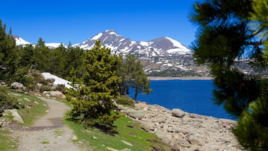 A mountain range with snow-capped peaks, a clear blue lake, and a rocky shoreline with a path leading to the water.