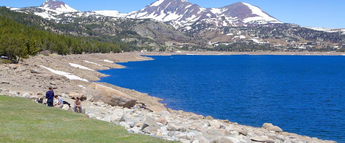 A rocky shoreline with a clear blue lake and snow-capped mountains in the background.