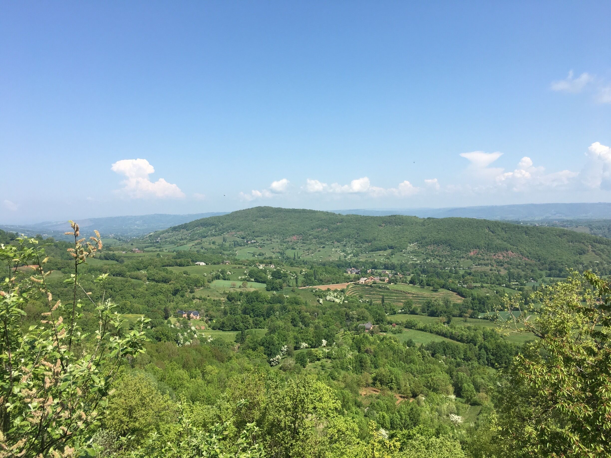 A lush green valley with rolling hills, scattered houses, and a clear blue sky.